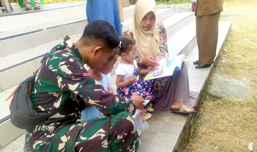Prada Adnan FZ, anggota Satgas TMMD ke-129 Kodim 0813/Bojonegoro, mendampingi anak-anak membaca buku dalam kegiatan Layanan Terpadu Perpustakaan Desa (LTPD) di Pendopo Balai Desa Kesongo, Kecamatan Kedungadem, Selasa (4/8/2026). Foto : Deni Aripandi/Sumber TMMD Bojonegoro