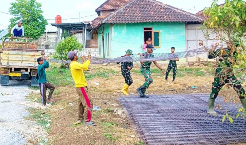 Personel Satgas TMMD bersama masyarakat bahu-membahu menurunkan material besi yang akan digunakan untuk pembangunan jalan cor beton di Dusun Kedungpandan, Rabu (22/7/2026).