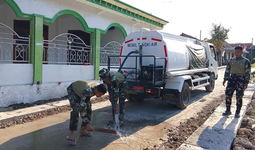 Anggota Satgas TMMD ke-129 Kodim 0813 Bojonegoro melakukan penyiraman atau curing jalan cor di Dusun Krebet, Desa Kesongo, Kecamatan Kedungadem, Kabupaten Bojonegoro, Minggu (09/08/2026). Foto: Deni Ari Pandi/Sumber: TMMD Bojonegoro.